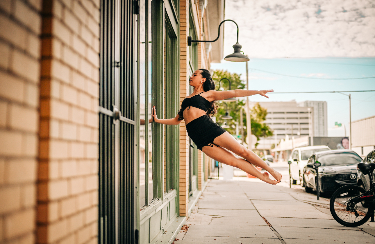 Arianna Luong in a horizontal leap beside a green storefront, arms extended
