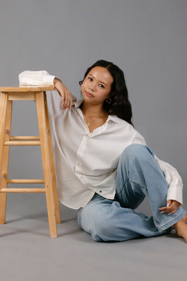 Arianna Luong seated on the studio floor leaning against a wooden stool